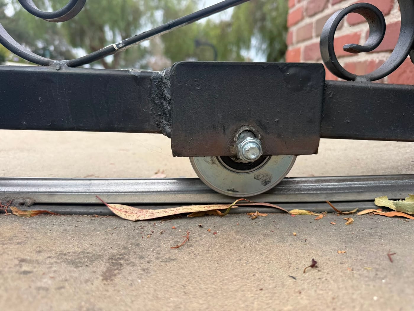 Close view of a slide gate roller sitting in its floor track beneath an ornamental iron gate