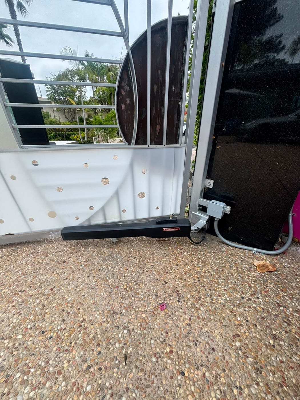 A LiftMaster swing gate operator arm fitted to a modern white and glass driveway gate