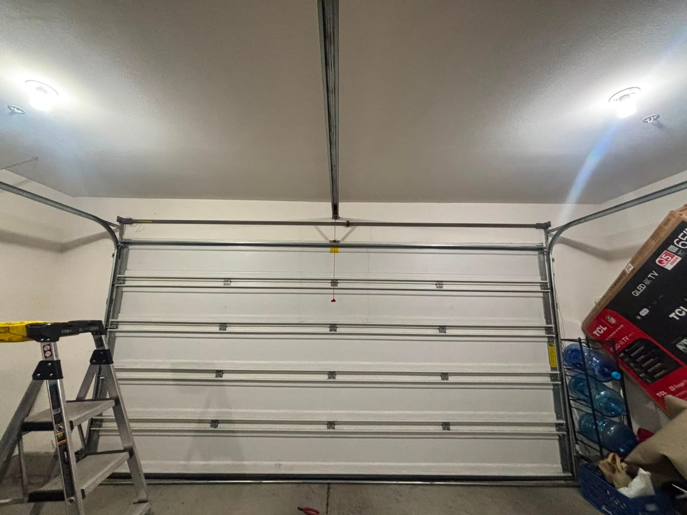 A newly installed white sectional garage door seen from inside the garage, showing the horizontal tracks, reinforcing struts and torsion bar above the opening