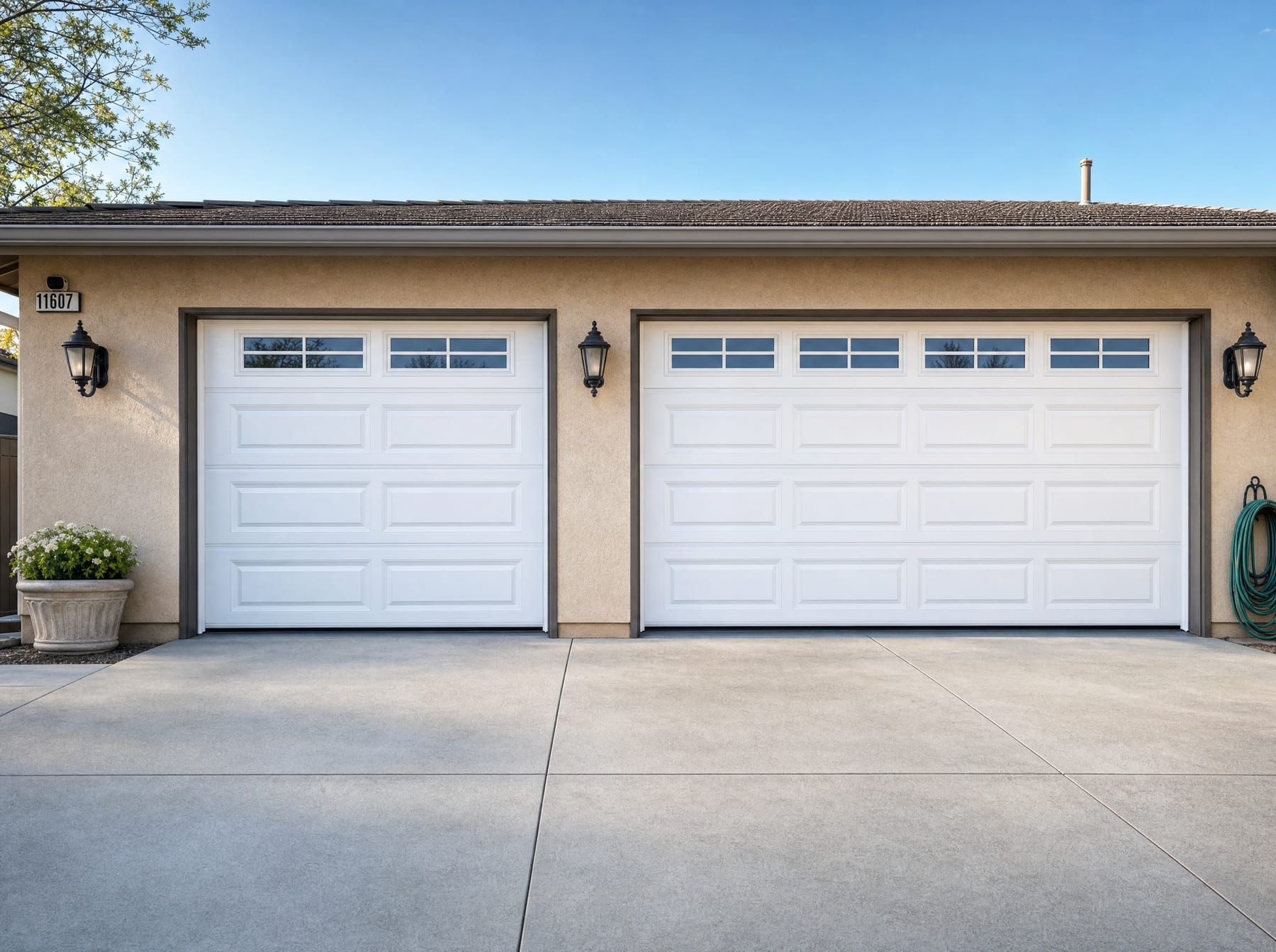 Two newly installed white raised-panel garage doors of different widths, each with a row of small window panes, on a tan stucco San Diego home with a composite shingle roof